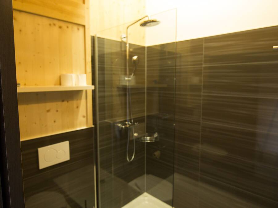 Un baño moderno con ducha envuelta en vidrio, inodoro blanco y estantes de madera.