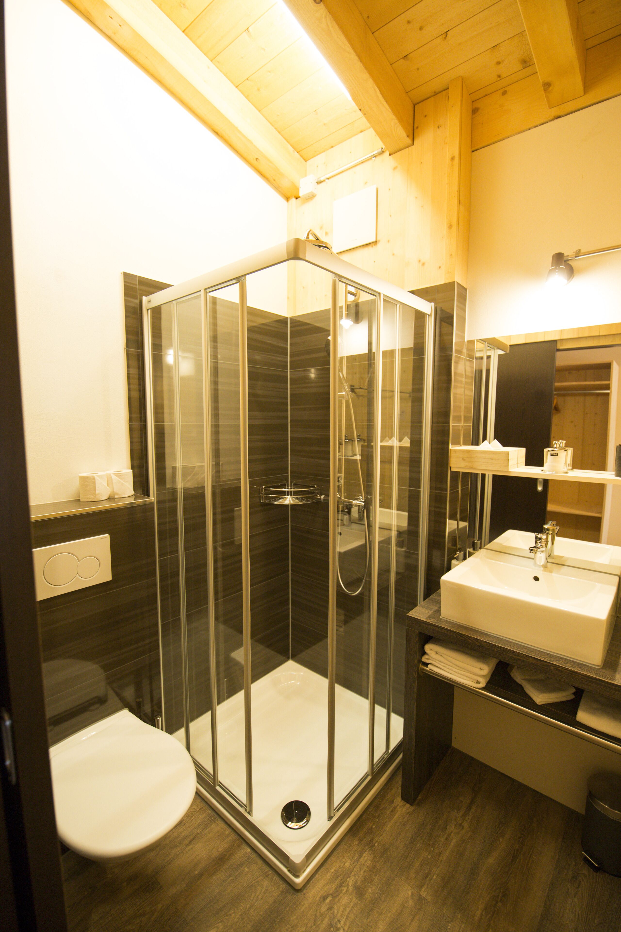 Un baño moderno con ducha de vidrio, inodoro y lavamanos con espejo.