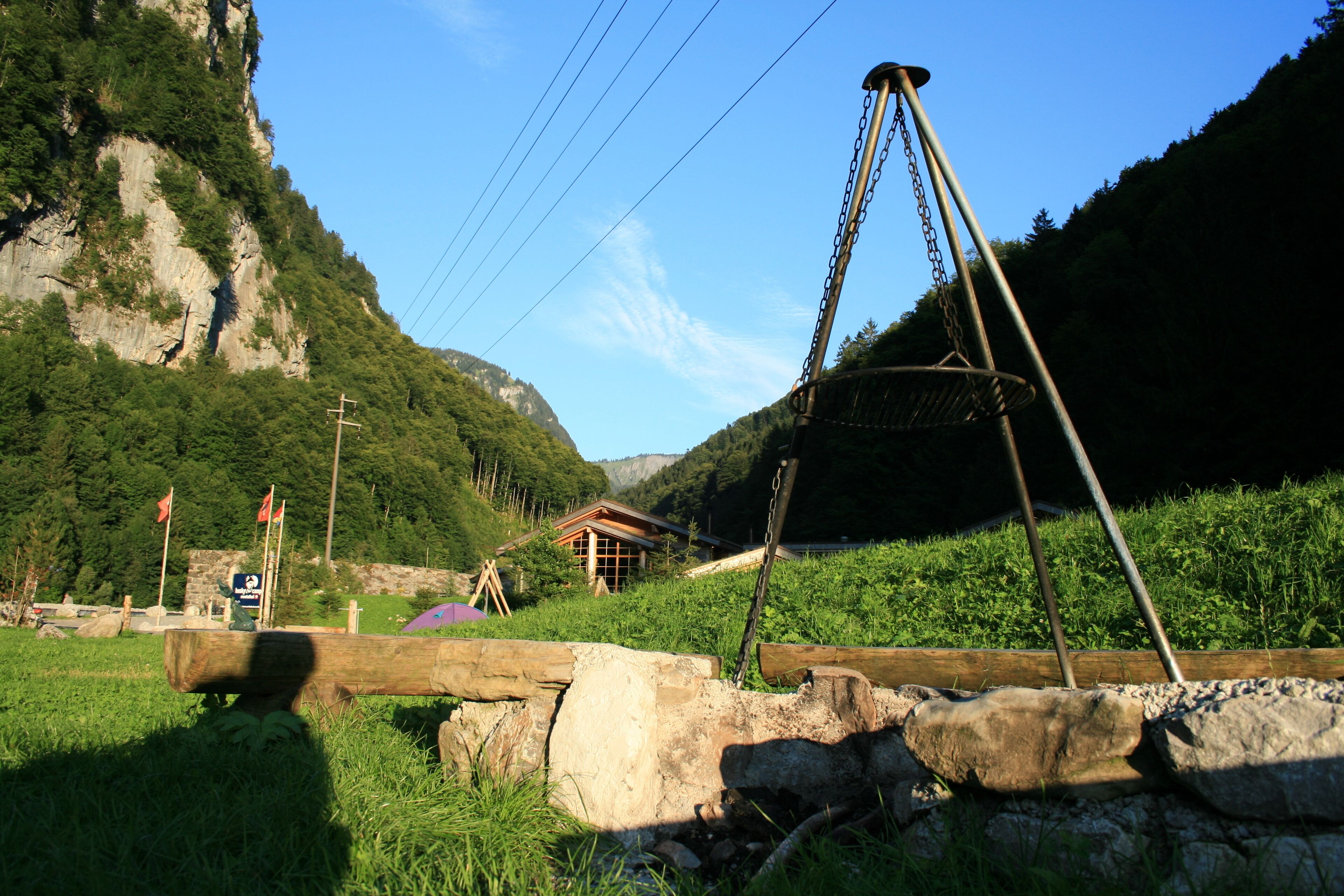 Una estructura rústica de madera con estructura metálica, rodeada de vegetación exuberante y un paisaje montañoso.