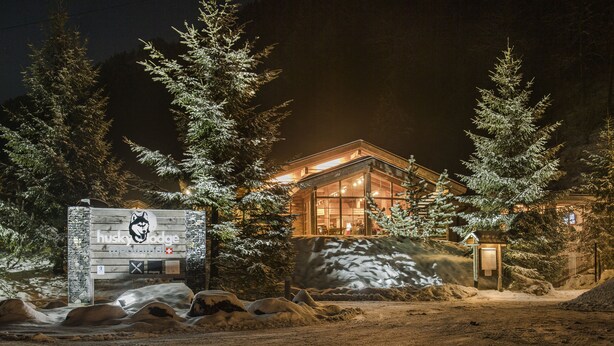 A lodge with a wooden exterior and glass walls, surrounded by snow-covered trees and rocks.
