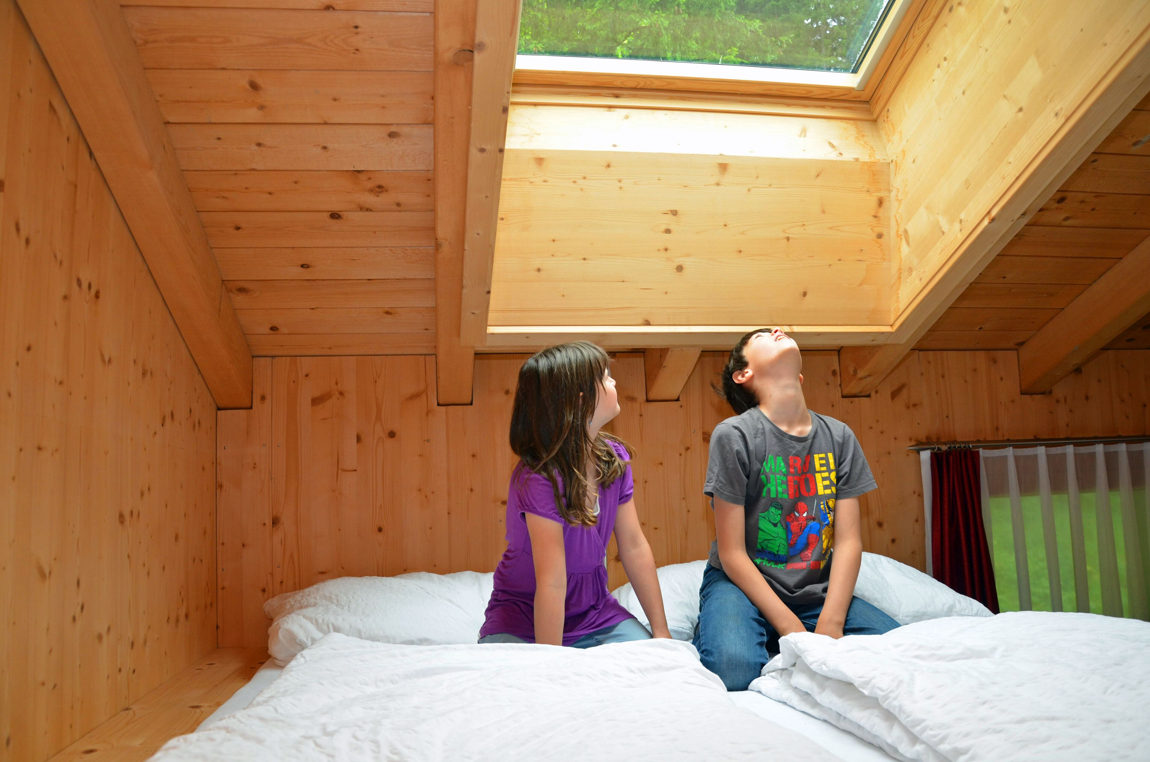 Ein Zimmer mit Holzboden, einem Oberlicht, einem Bett und einem Fenster mit Vorhängen.