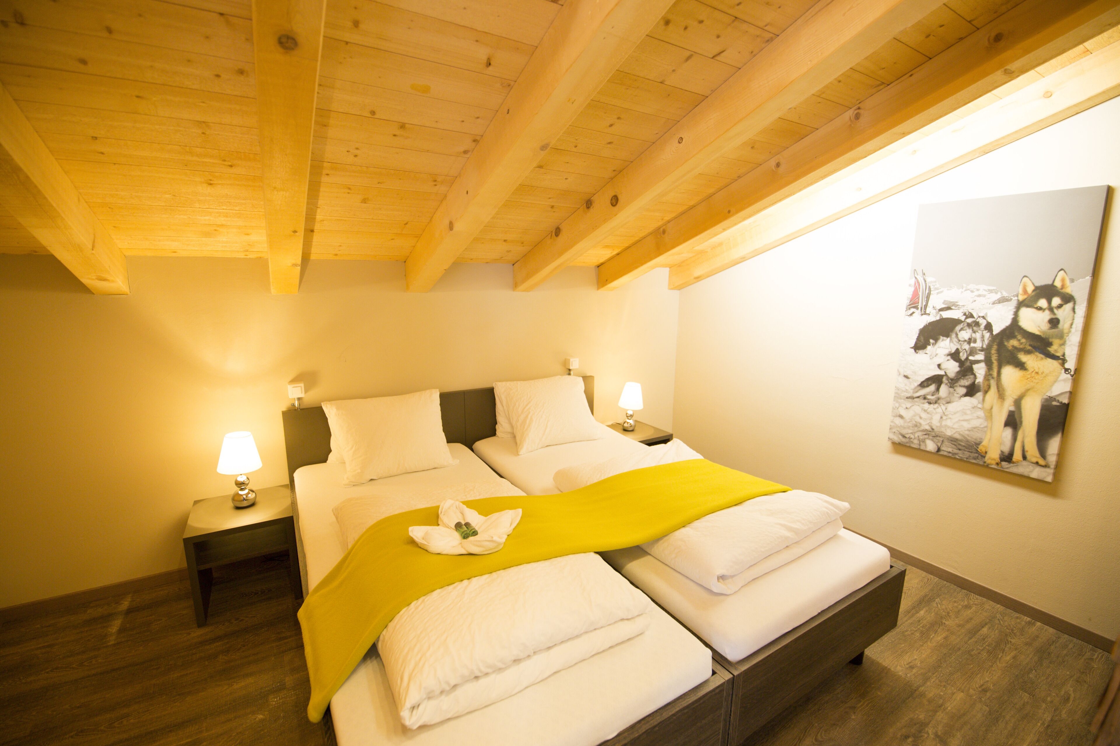 A hotel room with two beds, wooden ceiling beams, white bedding, and a painting of dogs on the wall.