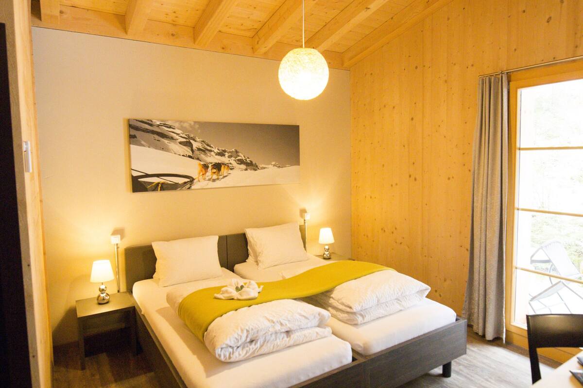 A wooden-paneled bedroom with a bed, bedside lamps, a painting, and a window with curtains.