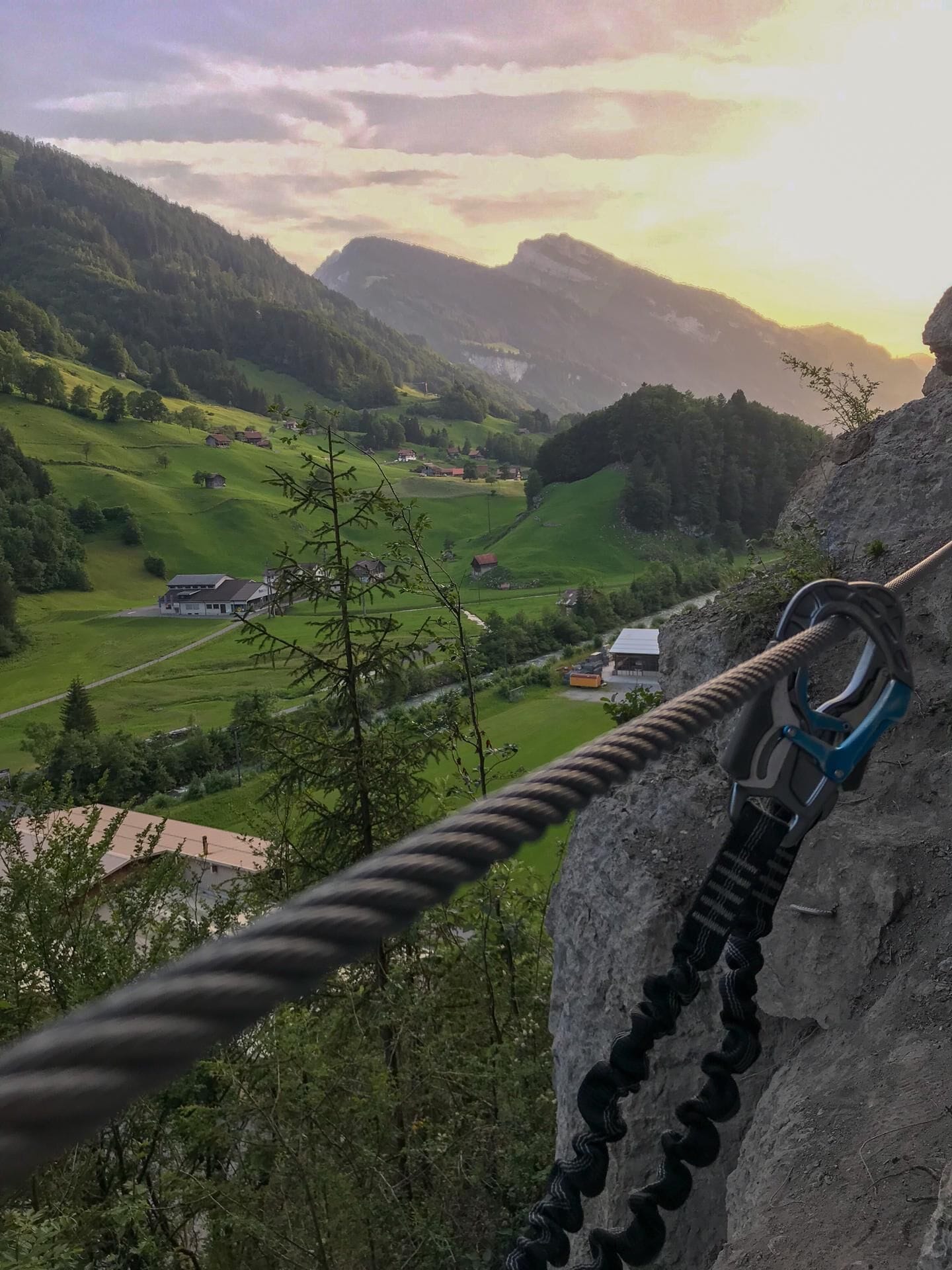 Eine Seilbrücke über ein Tal mit Häusern und viel Grün im Hintergrund.