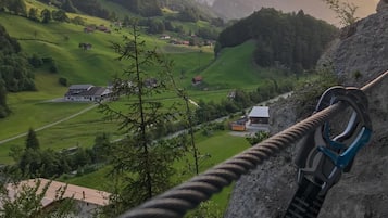 Eine Seilbrücke über ein Tal mit Häusern und viel Grün im Hintergrund.