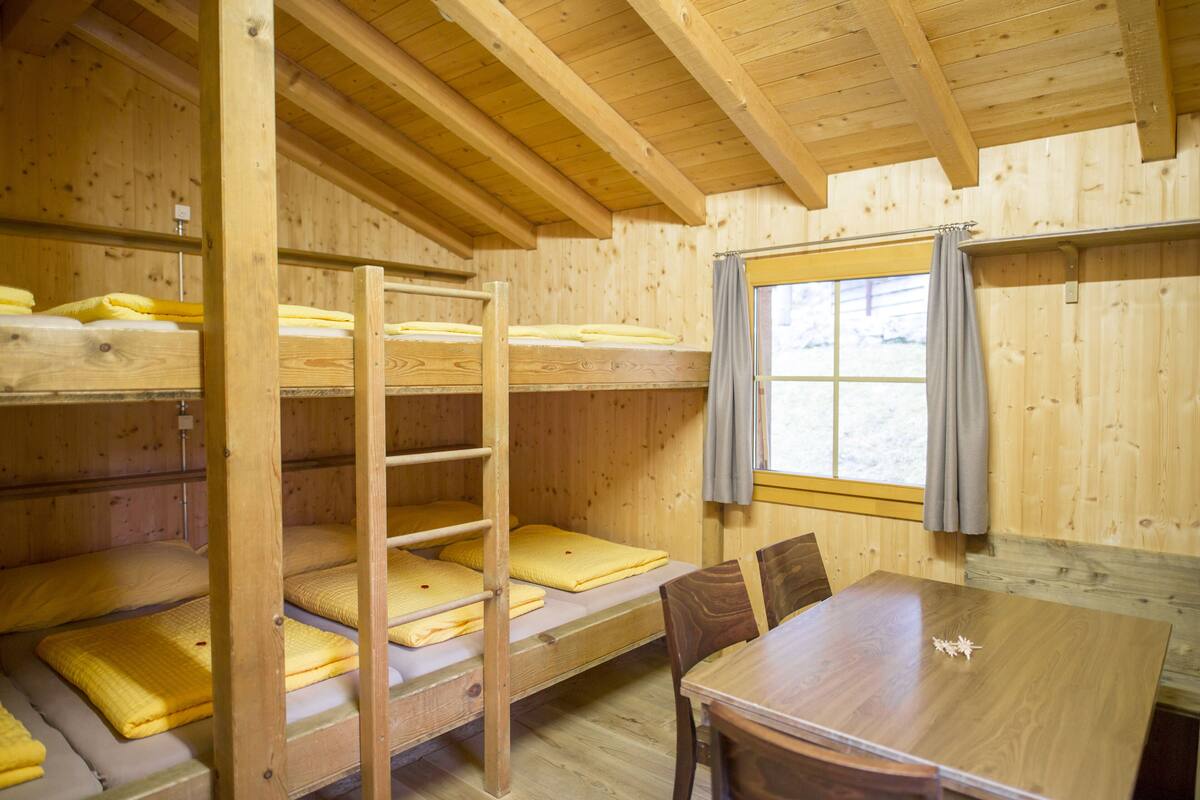 A wooden cabin with bunk beds, a dining table, and a window with curtains.