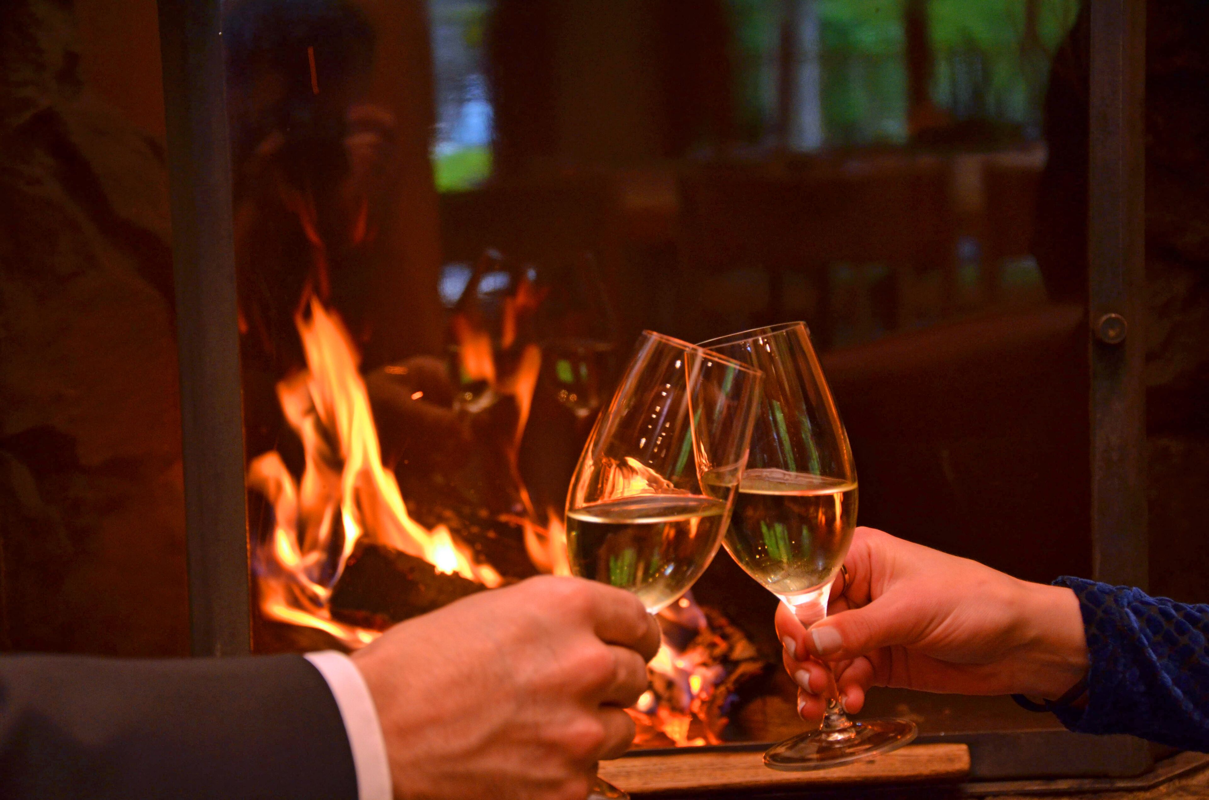 Deux mains tenant des verres à vin devant une cheminée.