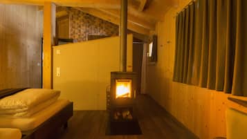 A cozy room with a wood-burning stove, a bed, and a window with curtains.