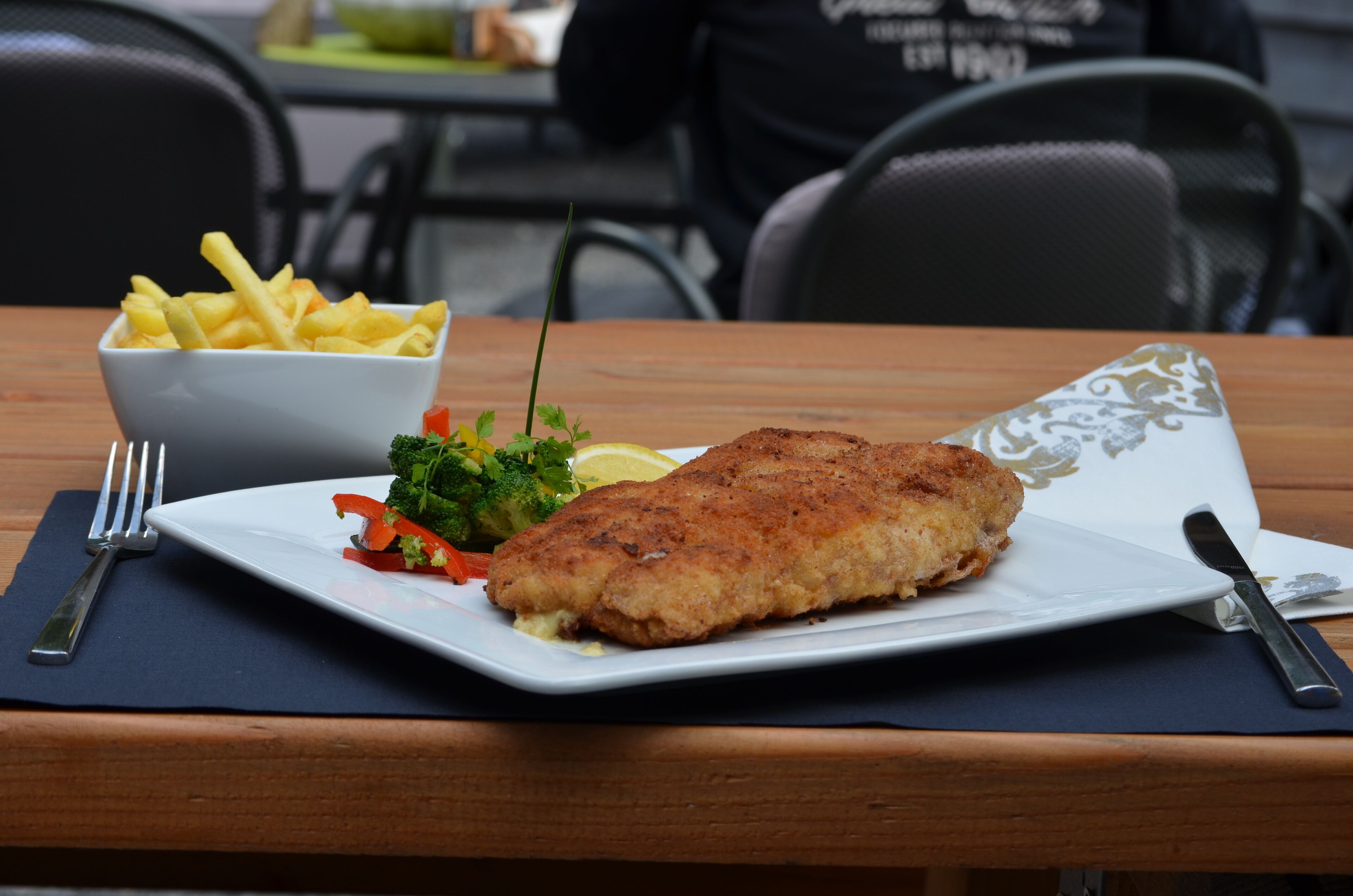 Un plato de pescado rebozado con vegetales y papas fritas sobre una mesa de madera.