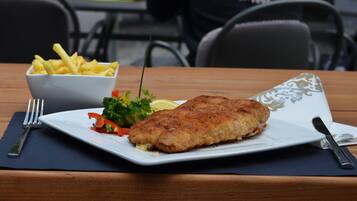 Un plato de pescado rebozado con vegetales y papas fritas sobre una mesa de madera.