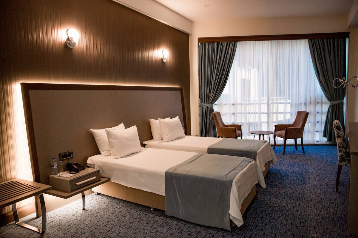 A hotel room with two beds, a desk, a chair, and a small table.