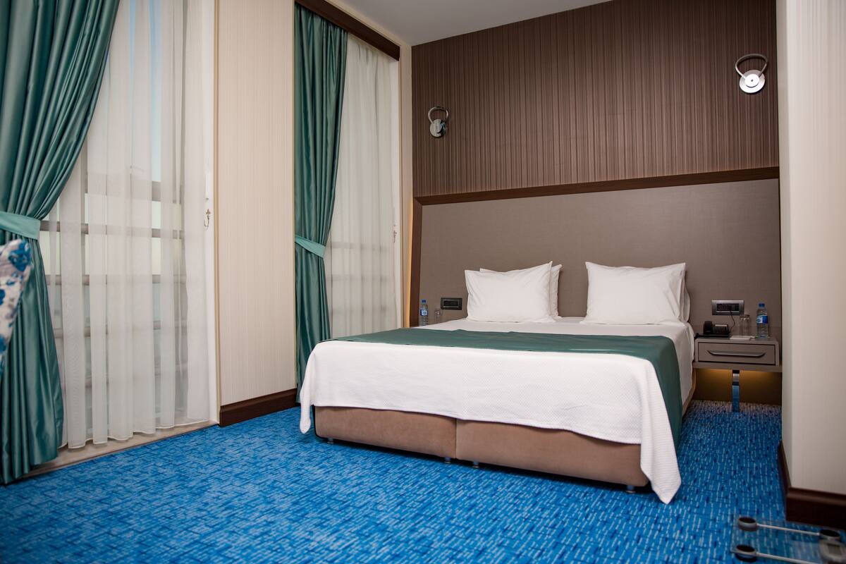 A hotel room with a large bed, a nightstand, a lamp, and a water bottle on the nightstand.
