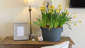 Un escritorio de madera con una lámpara, un cuadro enmarcado, una planta en maceta con flores amarillas y una silla de diseño vintage.