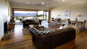 Amplia sala de estar con un sofá grande de cuero, un comedor con mesa y sillas de madera, y vistas al campo a través de puertas de vidrio amplias.