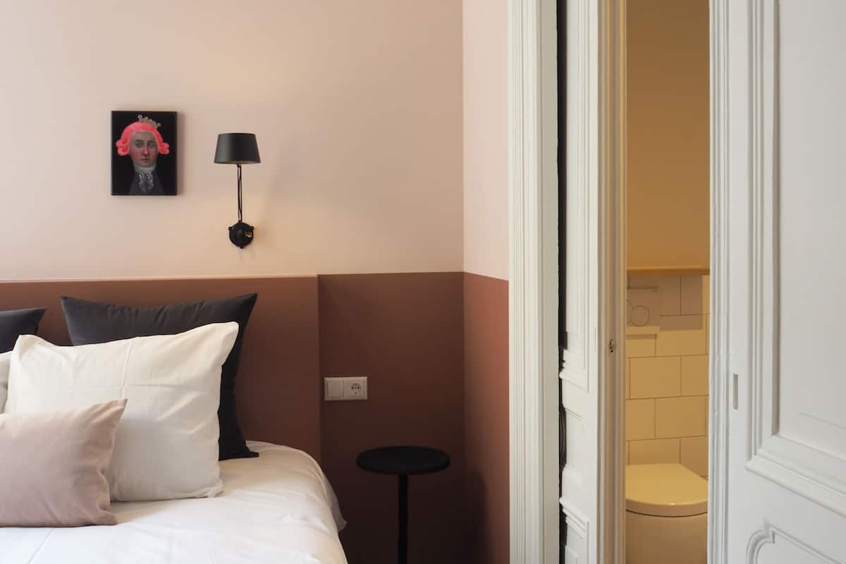 Une chambre d’hôtel avec un lit, des oreillers, une table de chevet, une lampe et un tableau au mur.