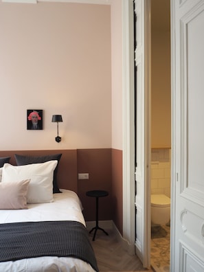 Habitación de hotel con cama, almohadas, mesita de noche, lámpara y un cuadro en la pared.