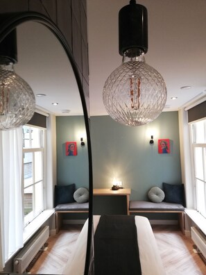 Een moderne slaapkamer met een grote spiegel, twee nachtkastjes met lampen, een bankje met kussens en een radiator.