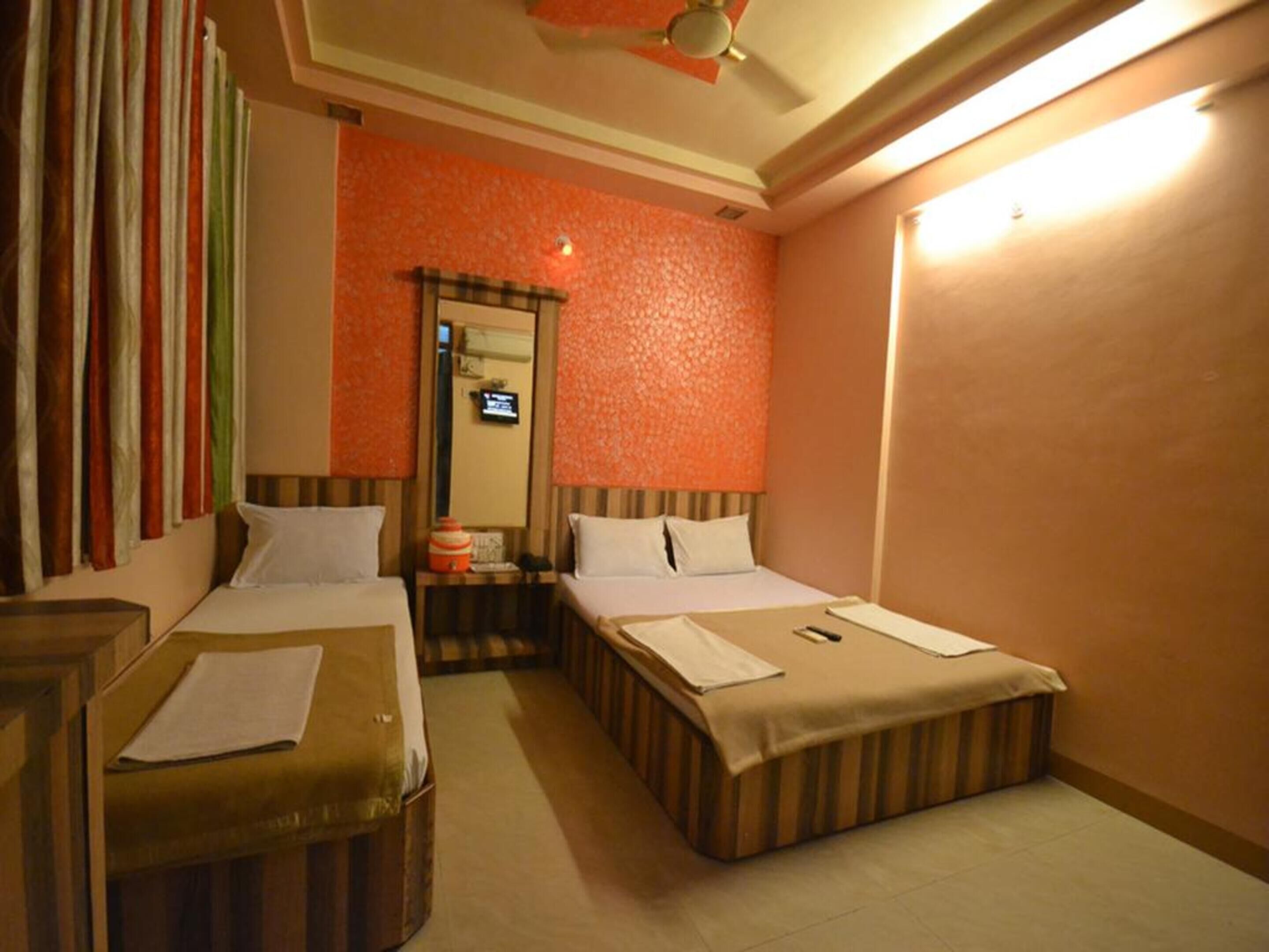 A hotel room with two beds, a small table, a mirror, and a ceiling fan.