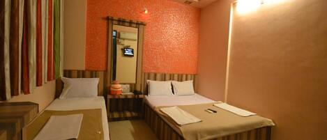 A hotel room with two beds, a small table, a mirror, and a ceiling fan.