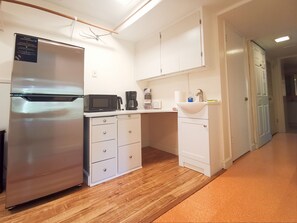 Cocina compacta con refrigerador, microondas, cafetera y lavabo con espejo.