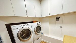 A compact laundry room with two front-loading washing machines, wooden flooring, and white cabinets. - POWER ON - The Forest Rooms -- A Peaceful Oasis close to everything (Issaquah)