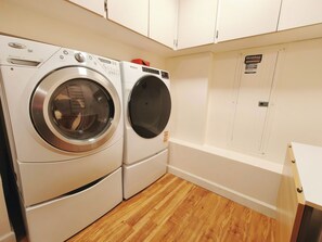 A laundry room with two front-loading washing machines, wooden flooring, and white cabinetry. - POWER ON - The Forest Rooms -- A Peaceful Oasis close to everything (Issaquah)