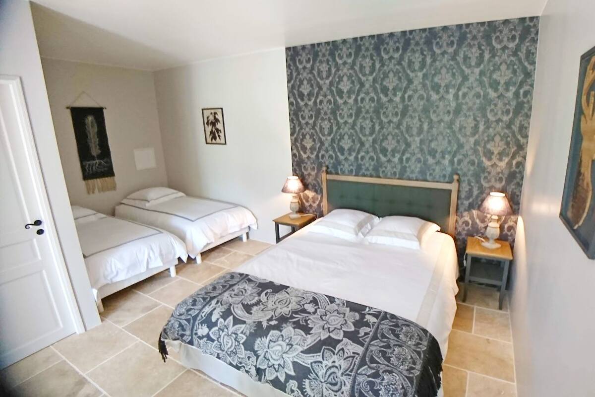Ein Hotelzimmer mit zwei Einzelbetten, einem Kingsize-Bett und einer gemusterten Tagesdecke. Es gibt zwei Nachttische mit Lampen.