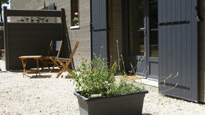 Een houten gebouw met een grindpad, een bloempot en twee houten stoelen.