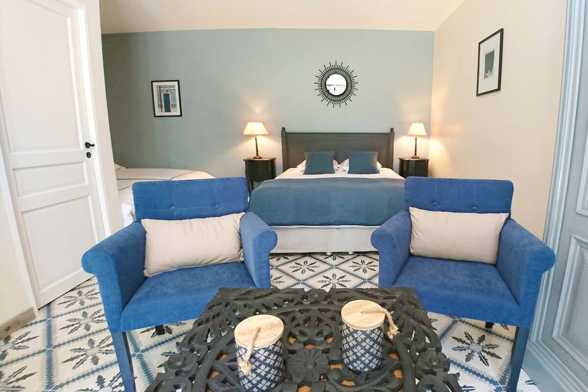 Ein Zimmer mit einem Bett, zwei blauen Sessel, einem Couchtisch mit Kerzen und einem Boden aus gemusterten Fliesen.
