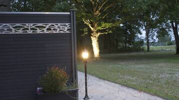 A building with a dark facade and a decorative white panel. There is a gravel path leading to a tree with a light illuminating its base.