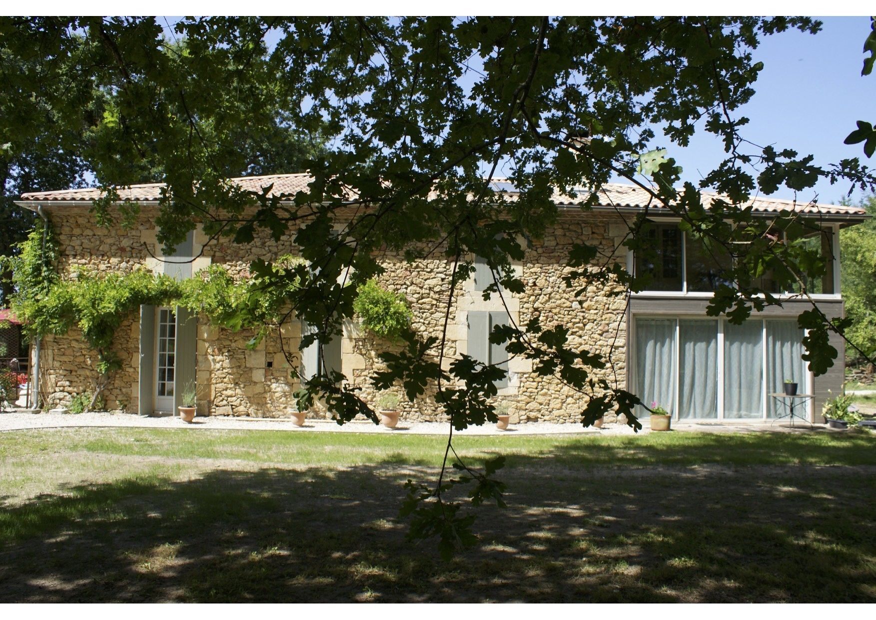 Una casa de pedra amb teulada de rajola, un garatge i un jardí davanter amb plantes en testos.