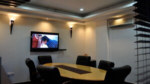 A conference room with a large table, black leather chairs, a flat-screen TV mounted on the wall, and an air conditioning unit. - Hotel Solo Victoria (New Delhi)