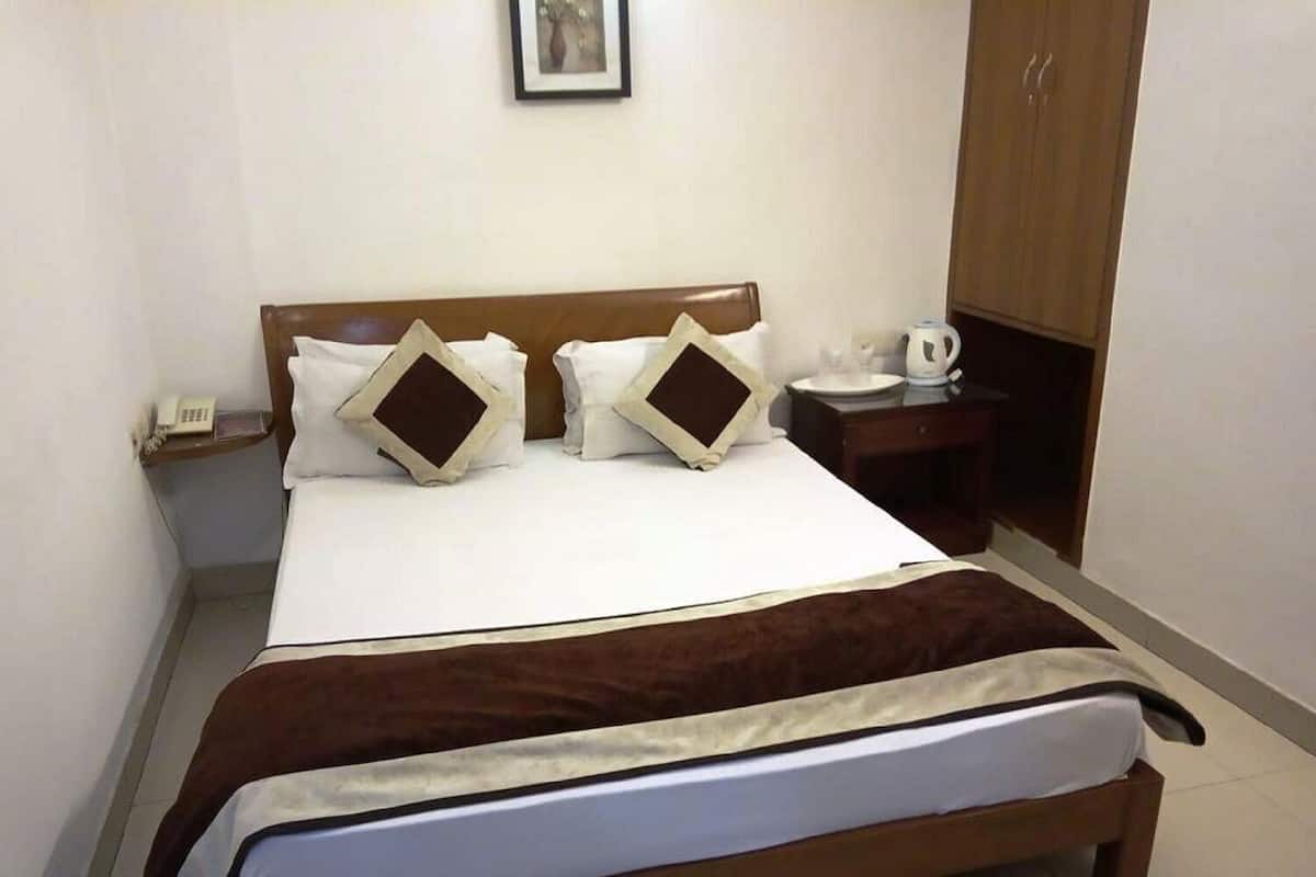 A hotel room with a bed, bedside table, a telephone, a framed picture on the wall, and a wardrobe.