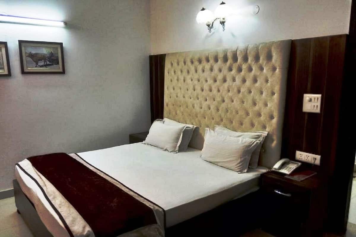 A neatly made bed with white linens and a red throw blanket, a wooden nightstand with a telephone, and a wall-mounted light fixture.