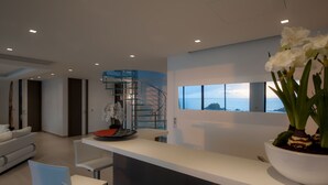 Un intérieur moderne avec un comptoir d’accueil blanc, un canapé blanc et un coin repas. Une grande fenêtre offre une vue sur la mer.