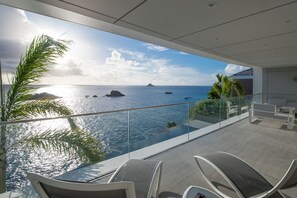 Un balcon moderne doté d’une balustrade en verre, offrant une vue sur une étendue d’eau et des îles lointaines.