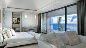 Une chambre d’hôtel moderne dotée d’un grand lit, d’un canapé, d’un bureau et d’un balcon offrant une vue sur l’océan.