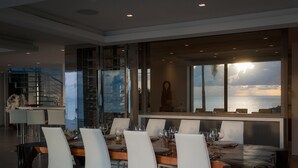 Un espace de restauration moderne avec vue sur l  ’océan, comprenant une longue table entourée de chaises blanches et d’une table en bois.