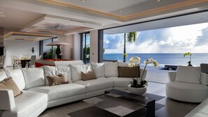 Un salon moderne avec un grand canapé d’angle blanc, une table basse et une vue sur l’océan.