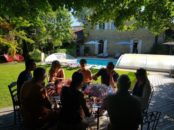 Um grupo de pessoas jantando ao ar livre em uma mesa, com uma piscina ao fundo.