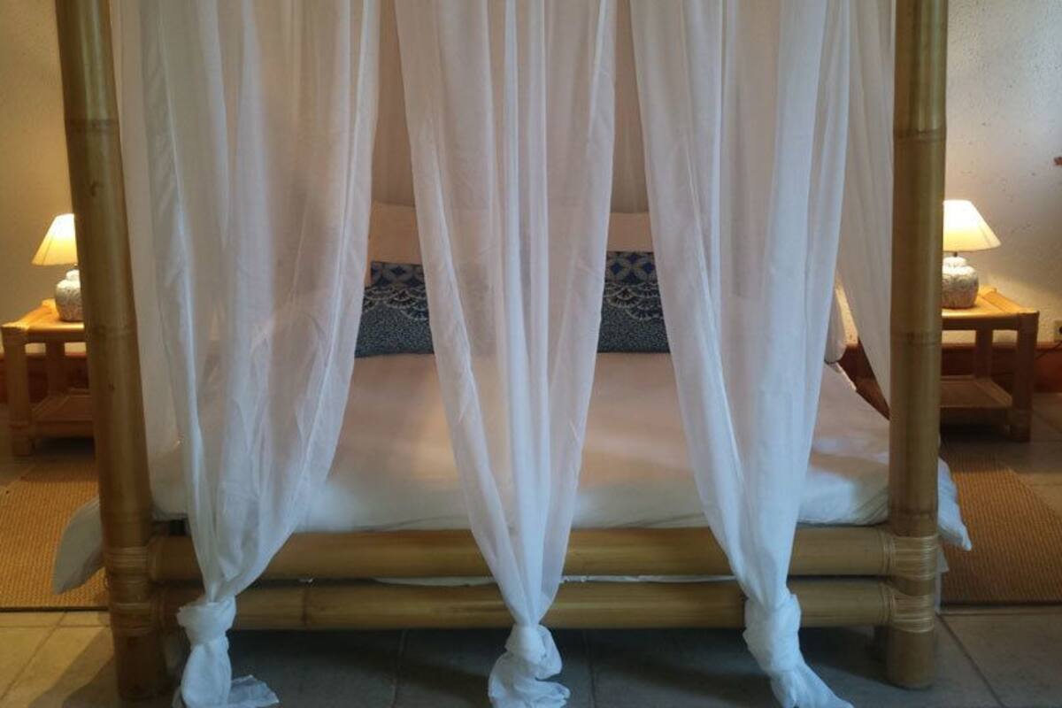 A four-poster bed with white drapes, a wooden headboard, and two bedside tables with lamps.
