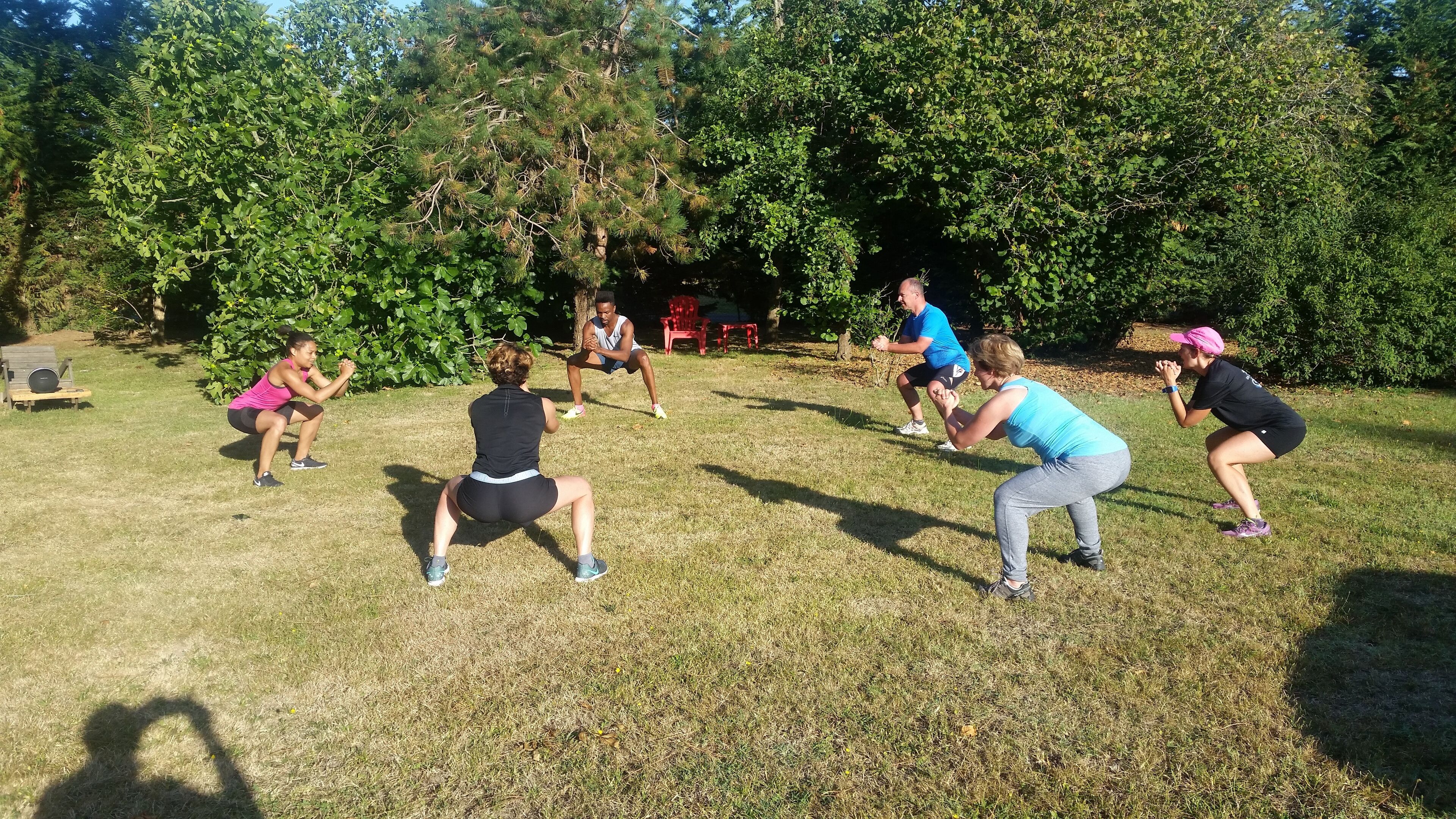 Un grup de persones fent exercici en una zona enjardinada a l'aire lliure, amb arbres al fons.