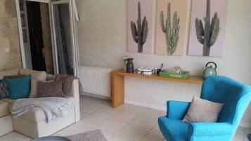 Un salón con sofá, un sillón azul, una mesa de centro y un radiador. Hay cuadros de cactus en la pared.
