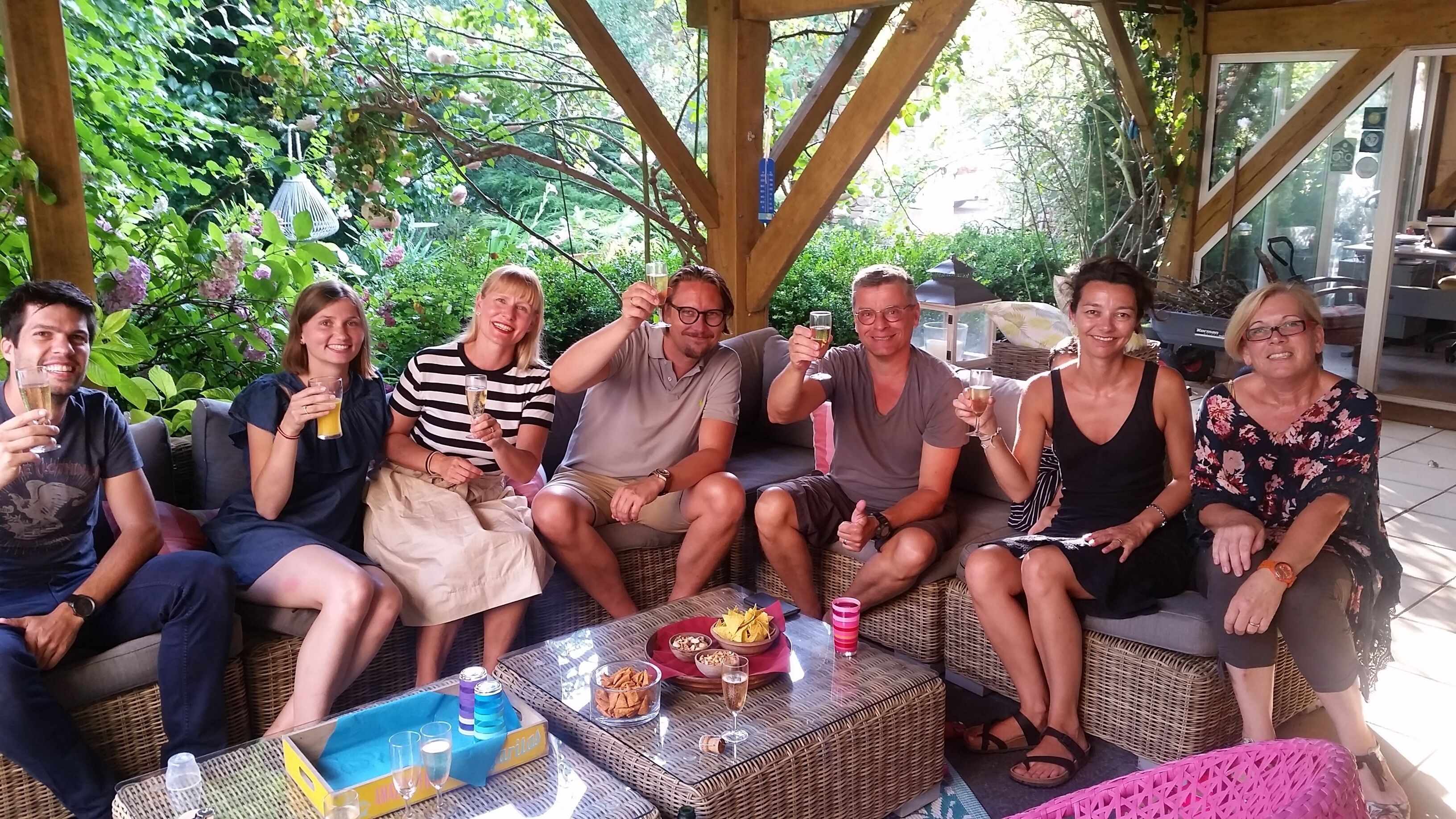 Eine Gruppe von Personen sitzt draußen auf Korbmöbeln, vor ihnen steht ein Tisch mit Getränken und Snacks.
