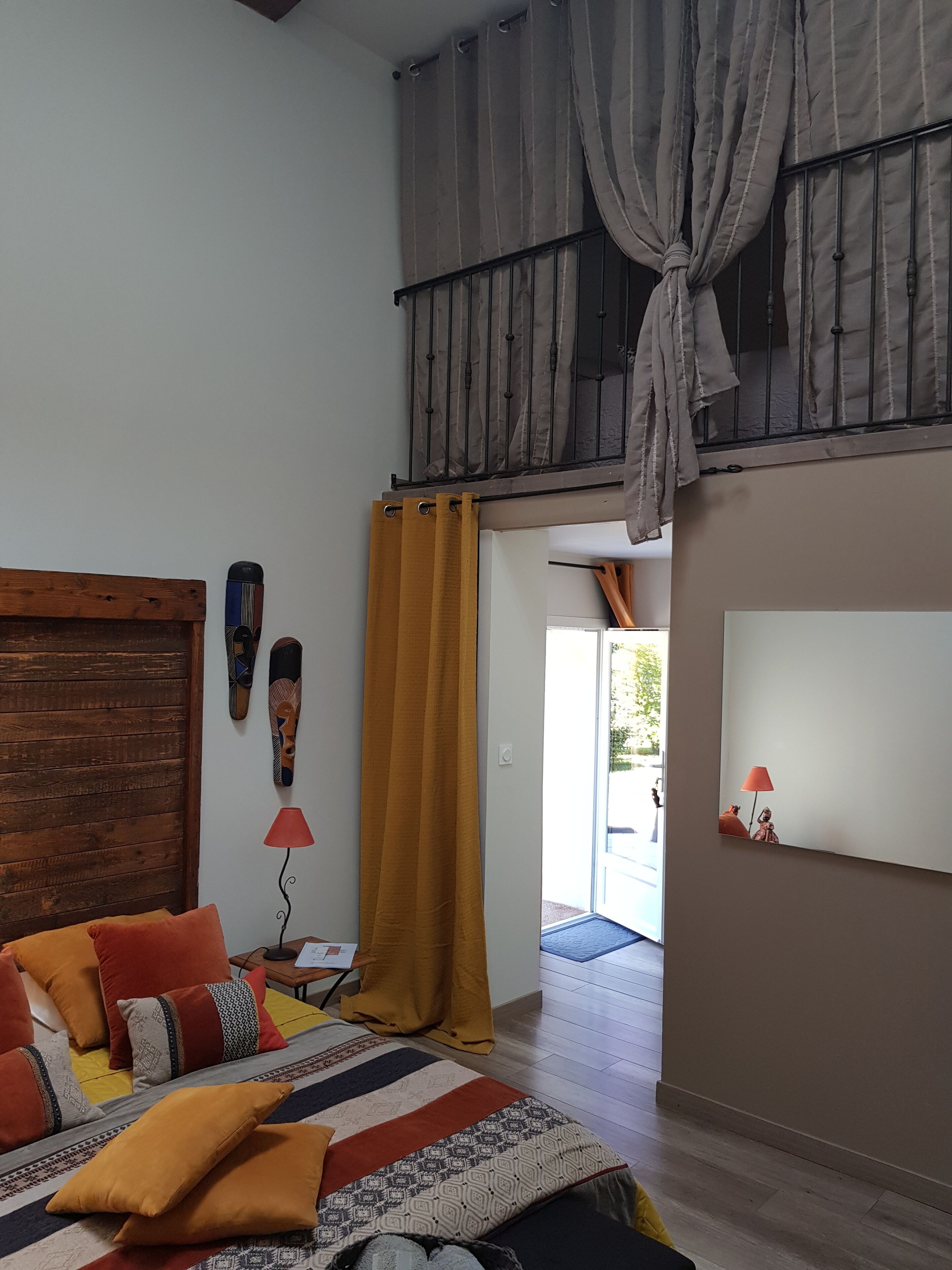 Een slaapkamer met een bed, een houten hoofdbord, een geel gordijn en uitzicht op het omliggende landschap.