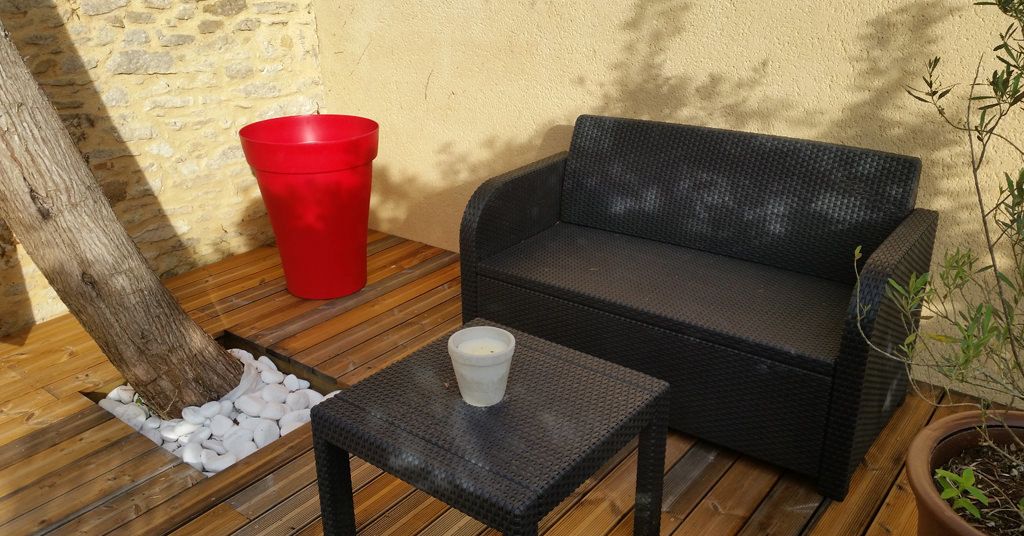 A wicker sofa and a small table with a glass on a wooden deck.