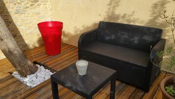 A wicker sofa and a small table with a glass on a wooden deck.