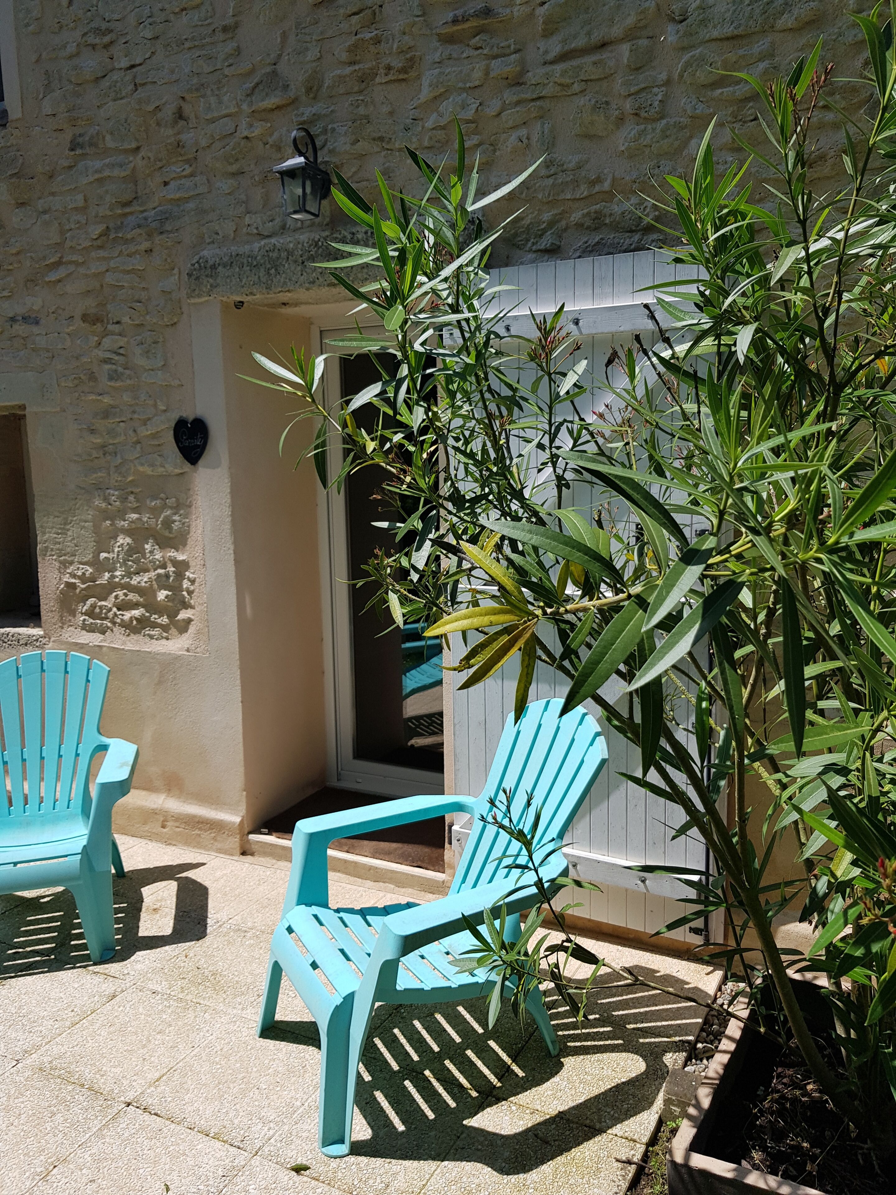 A patio area with two turquoise Adirondack chairs, a potted plant, and a stone wall.