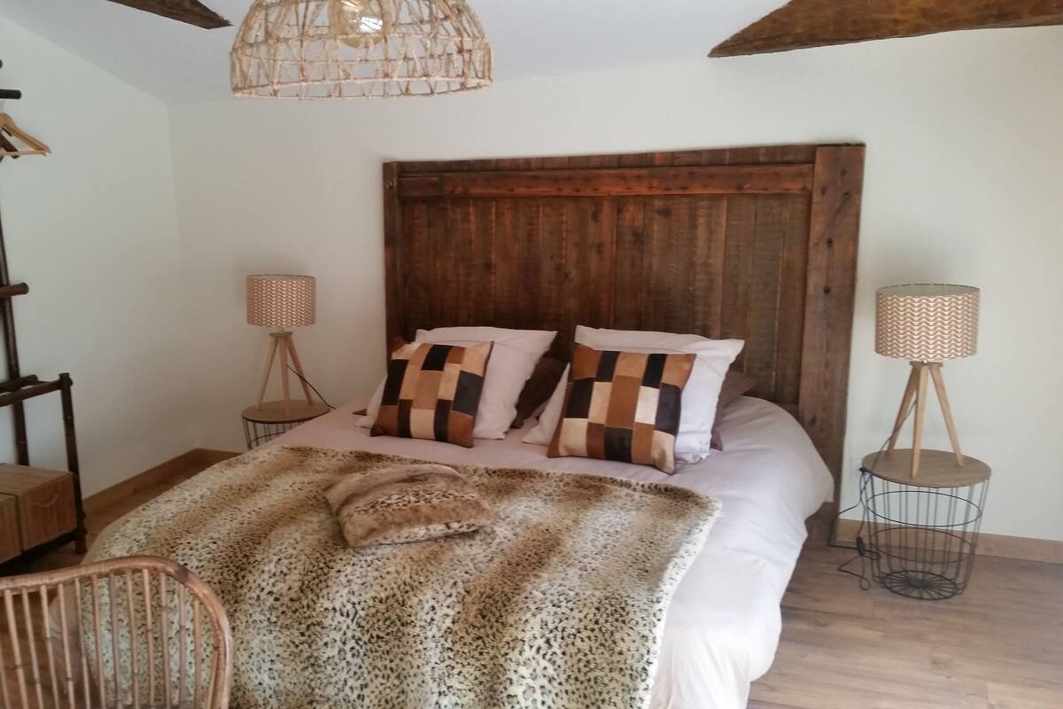 A bedroom with a wooden headboard, a bed with patterned pillows, a wooden chair, and two floor lamps.