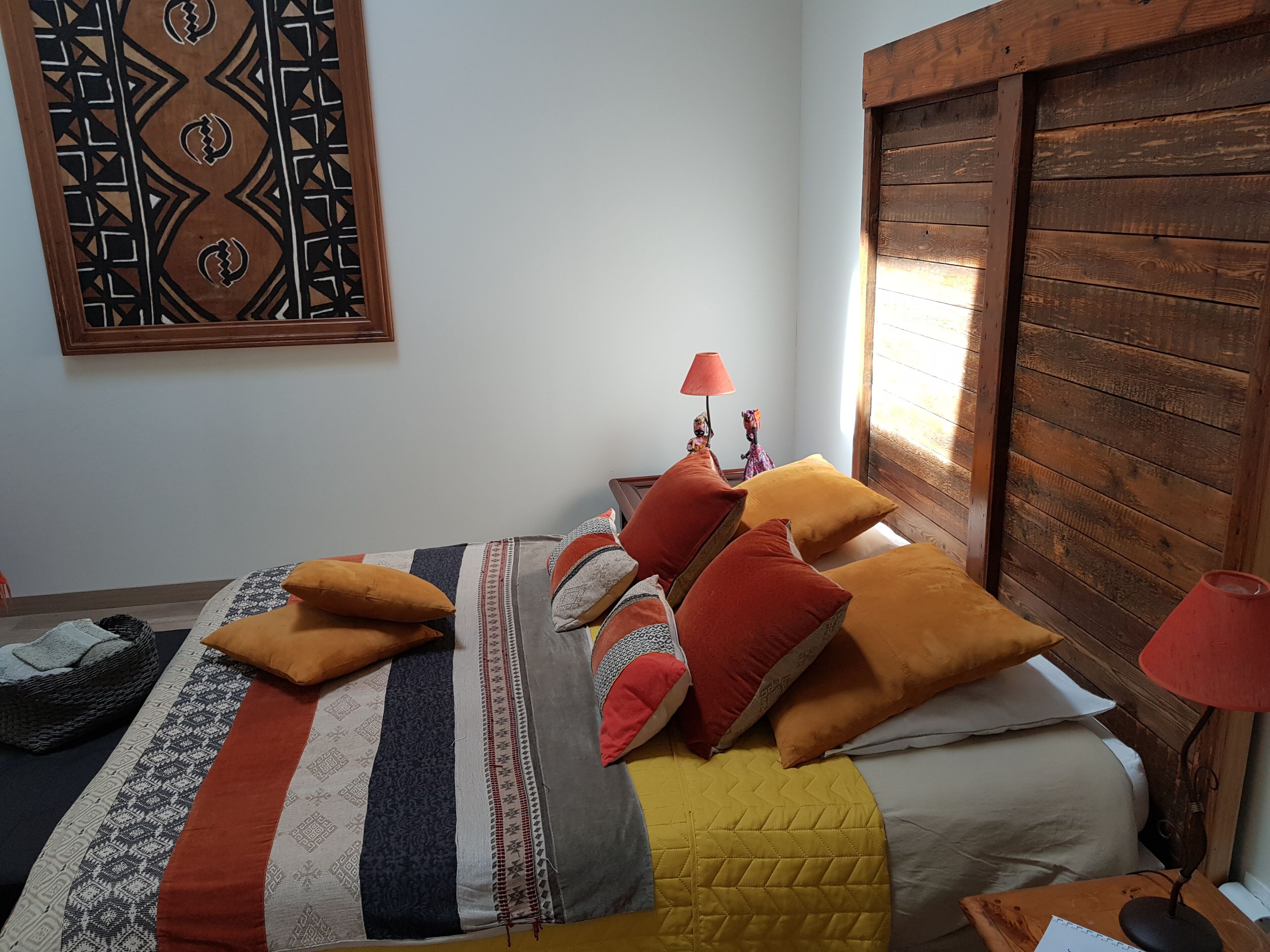 Un dormitorio con cama, almohadas, una lámpara y una obra de arte en la pared.